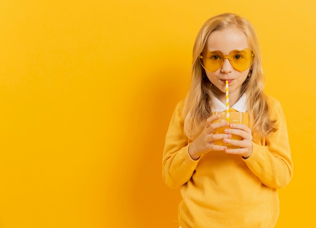 Foto gratuita vista frontal de la niña posando mientras bebe jugo y usa gafas de sol