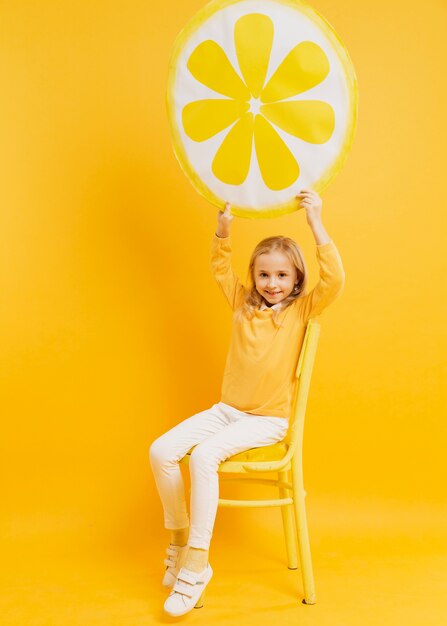 Vista frontal de la niña posando mientras sostiene la decoración de rodaja de limón