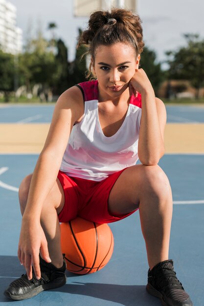 Vista frontal de la niña sentada en la pelota de baloncesto