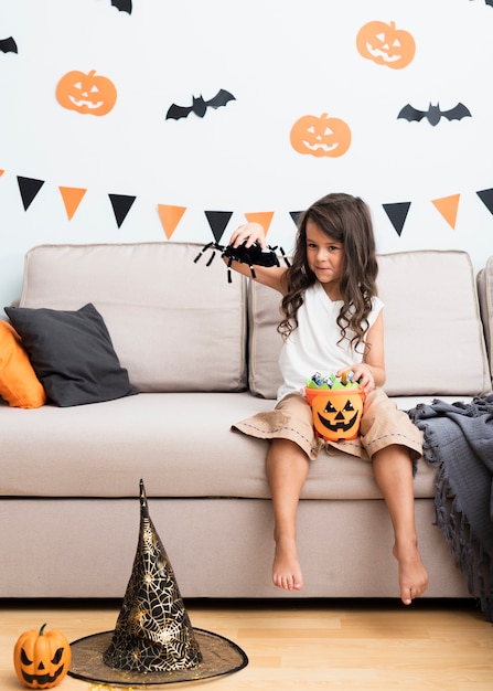 Vista frontal niña sentada en el sofá en halloween