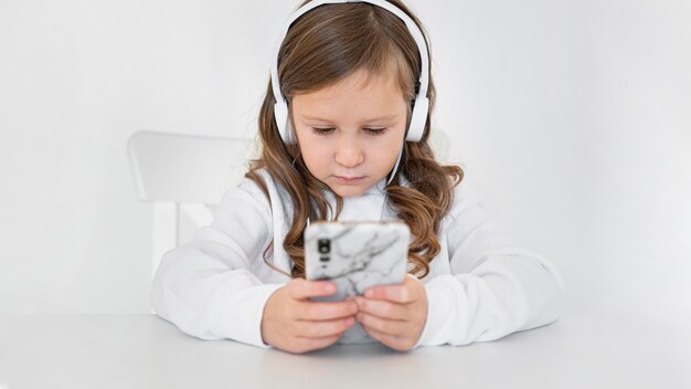 Vista frontal de la niña con smartphone y auriculares en casa