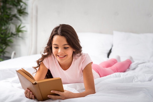 Foto gratuita vista frontal niña sonriente en casa leyendo en la cama