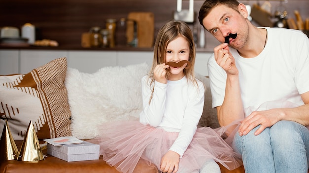 Vista frontal de la niña sonriente en falda tutú y padre con bigotes falsos