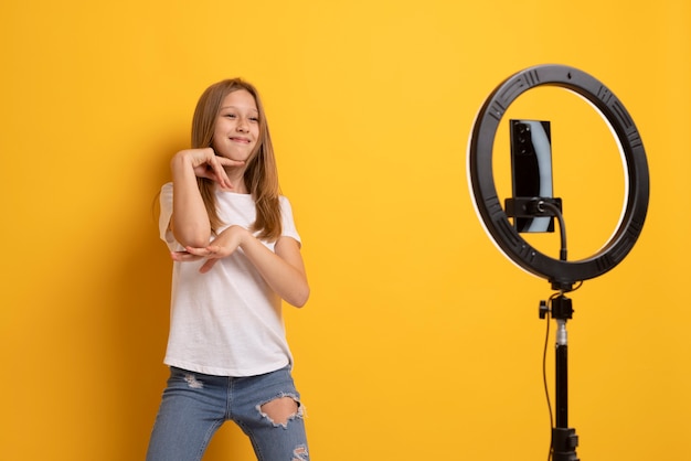 Vista frontal niña sonriente grabando con anillo de luz