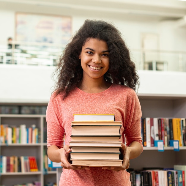 Vista frontal niña sonriente con pila de libros