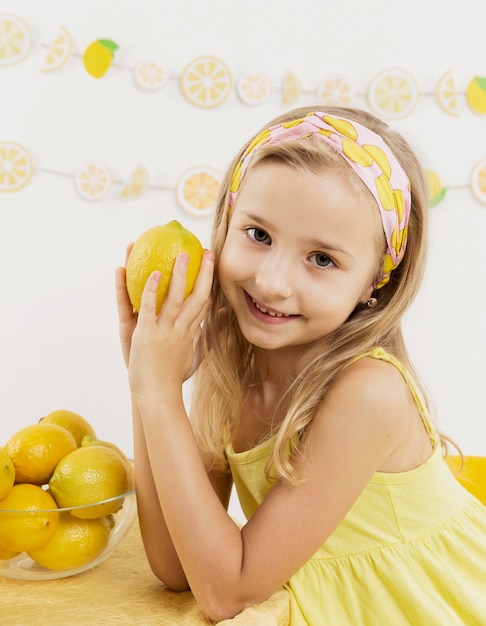 Foto gratuita vista frontal de la niña sonriente posando mientras sostiene un limón