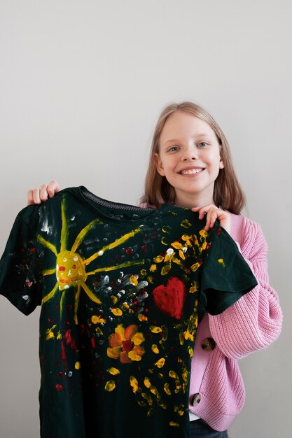 Vista frontal de una niña sosteniendo una camiseta pintada con bricolaje