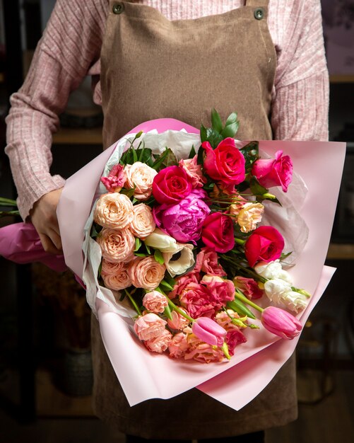 Vista frontal niña sostiene hermoso ramo de rosas coloridas tulipanes y peonías en una envoltura de papel