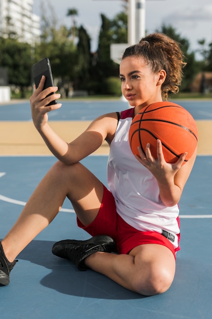 Vista frontal de la niña tomando selfie con pelota de baloncesto