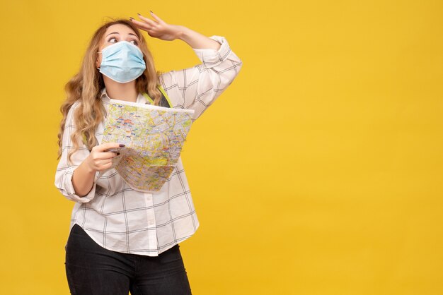 Vista frontal de la niña viajera concentrada con su máscara y mochila con mapa en amarillo