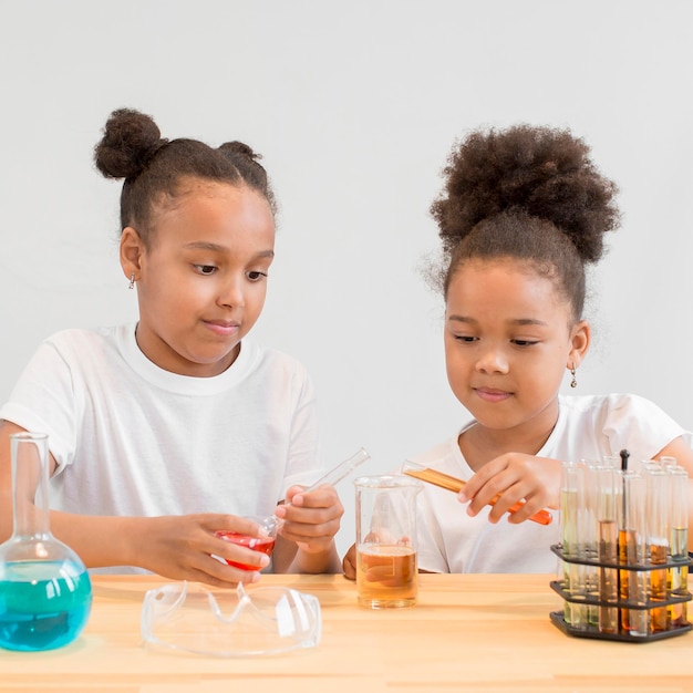 Vista frontal de niñas llevando experimentos de química con tubos y pociones.