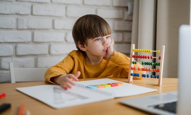 Vista frontal del niño con ábaco aprendiendo de la computadora portátil en casa