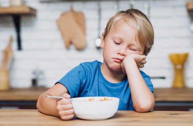 Vista frontal niño cansado tratando de comer sus cereales