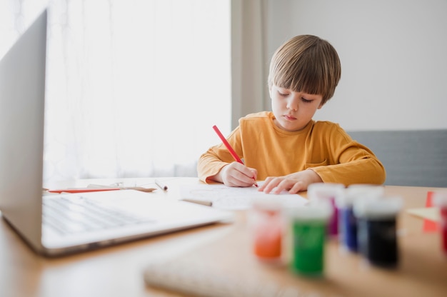 Vista frontal del niño en casa dibujando con la ayuda de una computadora portátil