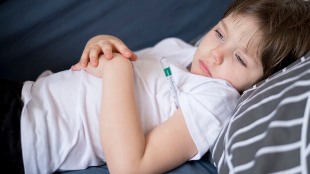 Vista frontal del niño enfermo sentado en la cama