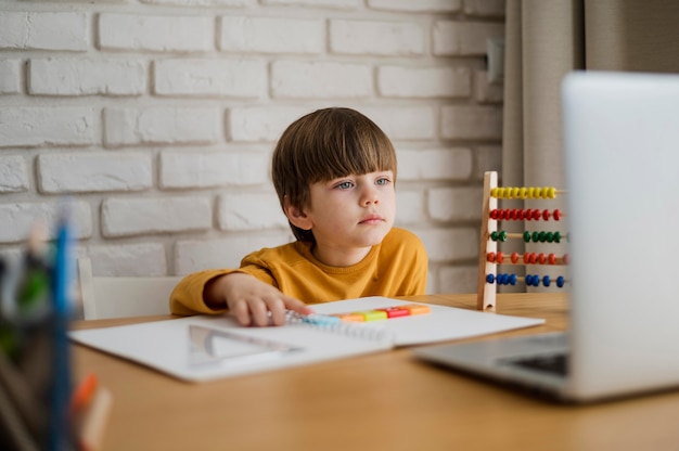 Vista frontal del niño en el escritorio aprendiendo de la computadora portátil