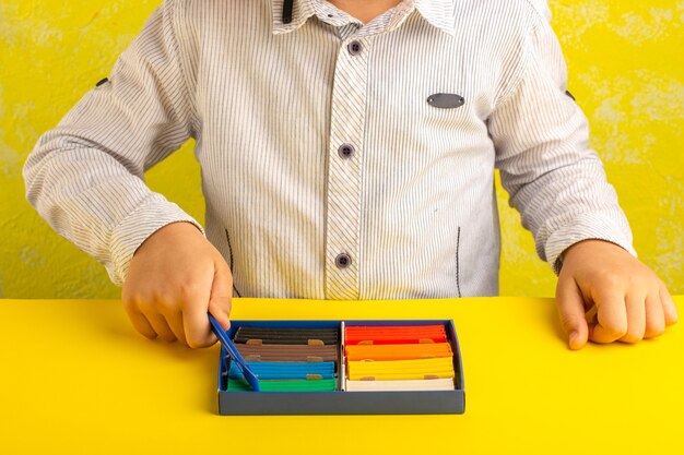 Vista frontal niño jugando con plastilinas de colores sobre superficie amarilla