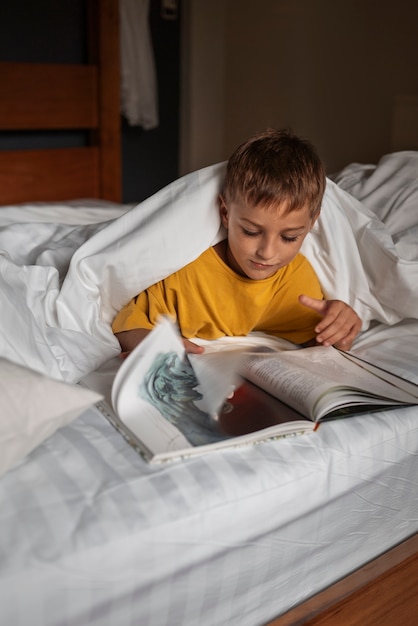 Vista frontal niño leyendo revista en la cama