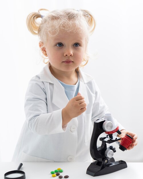 Vista frontal del niño lindo con bata de laboratorio y microscopio
