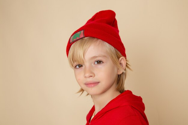 Vista frontal niño lindo en camisa roja y gorra en la pared blanca