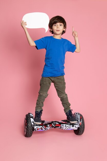 Una vista frontal niño lindo en camiseta azul y pantalones de color caqui montando segway en el espacio rosa