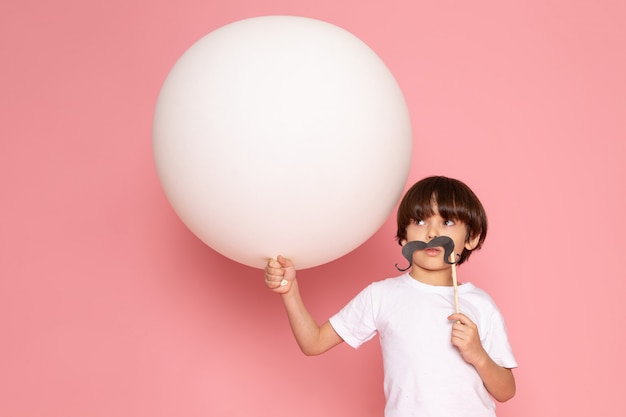 Una vista frontal niño lindo niño en camiseta blanca con bola blanca sobre el escritorio rosa