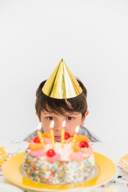 Foto gratuita vista frontal de un niño mirando pastel de cumpleaños y velas iluminadas