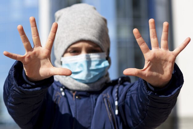 Vista frontal del niño mostrando las manos mientras usa una máscara médica afuera