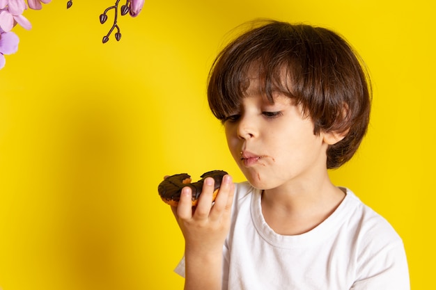 Foto gratuita una vista frontal niño niño en camiseta blanca comiendo donas en el piso amarillo