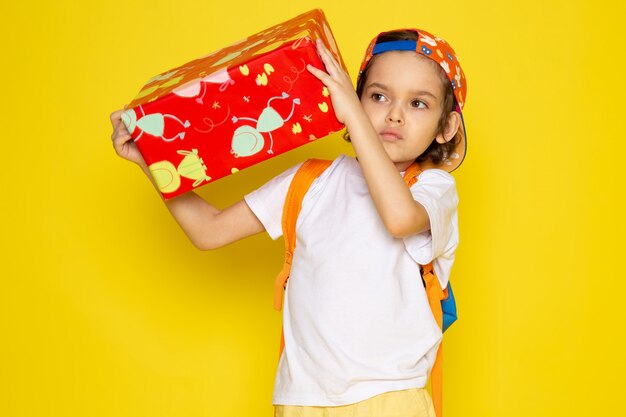 Vista frontal niño niño en camiseta blanca y gorra de béisbol con rojo diseñado presente en escritorio amarillo