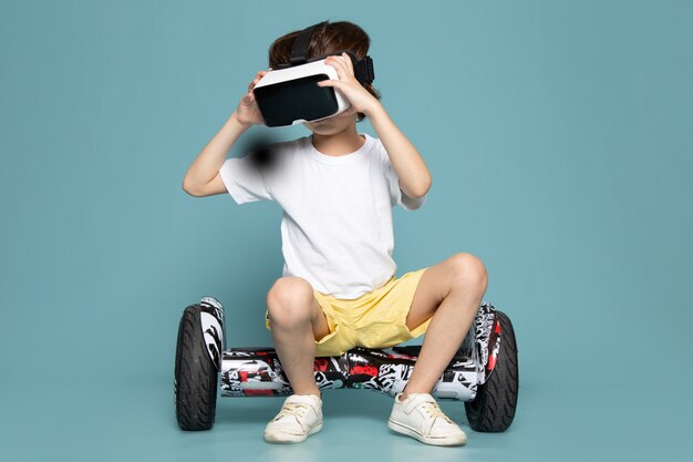 Una vista frontal niño niño en camiseta blanca jugando vr en segway en el espacio azul