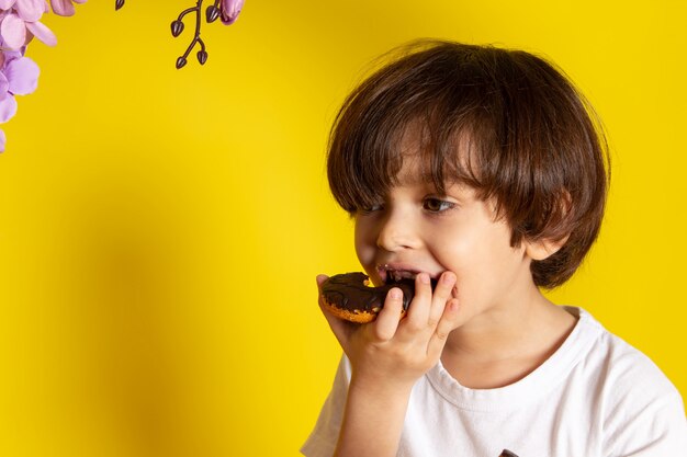 Una vista frontal niño niño comiendo donas con chocolate en el espacio amarillo