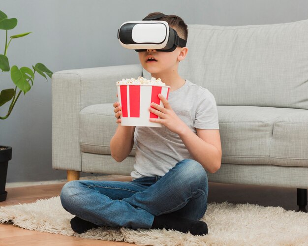 Vista frontal del niño con palomitas viendo películas usando auriculares de realidad virtual