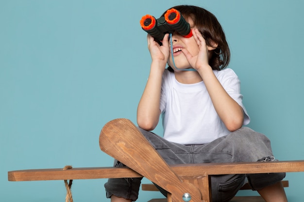 Foto gratuita vista frontal del niño pequeño en camiseta blanca con binoculares en el escritorio azul