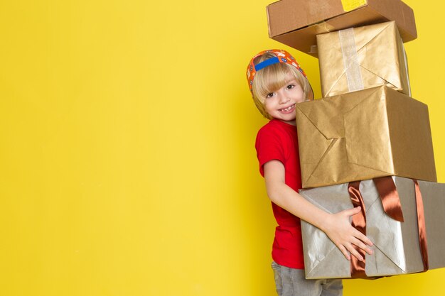 Una vista frontal del niño pequeño en la camiseta roja colorida gorra y jeans grises con cuadro sobre el fondo amarillo