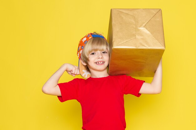 Una vista frontal del niño pequeño en la camiseta roja colorida gorra y jeans grises con cuadro sobre el fondo amarillo