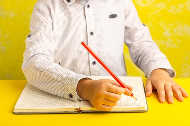 Vista frontal niño pequeño escribiendo y dibujando sobre superficie amarilla