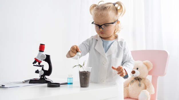 Vista frontal del niño pequeño lindo que aprende ciencia con plantas y microscopio