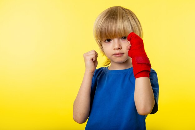 Una vista frontal niño pequeño niño posando boxeo en camiseta azul en la pared amarilla