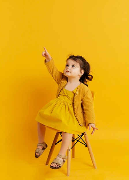 Vista frontal del niño posando mientras está sentado en la silla y apuntando hacia arriba