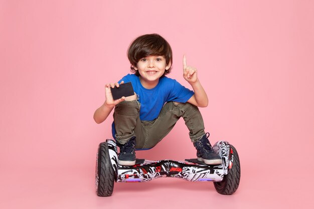 Una vista frontal niño sonriente en camiseta azul montando segway en el piso rosa