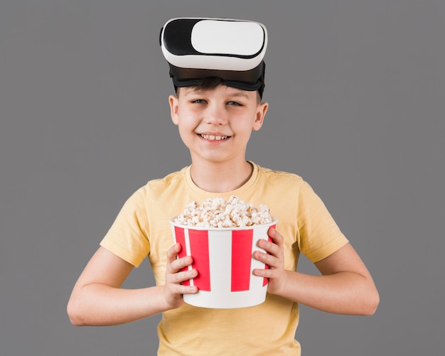 Vista frontal del niño sonriente con casco de realidad virtual con palomitas de maíz