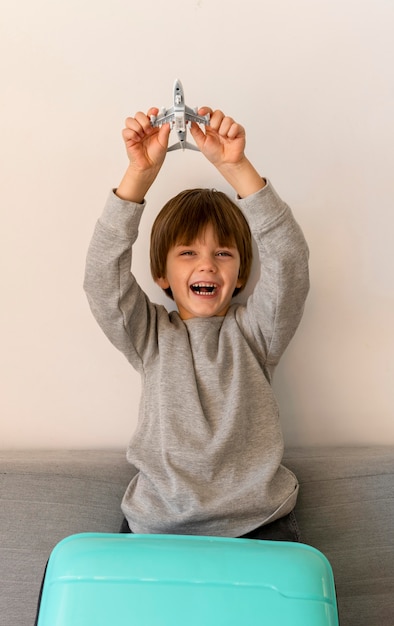 Vista frontal del niño sonriente con equipaje y figurilla de avión