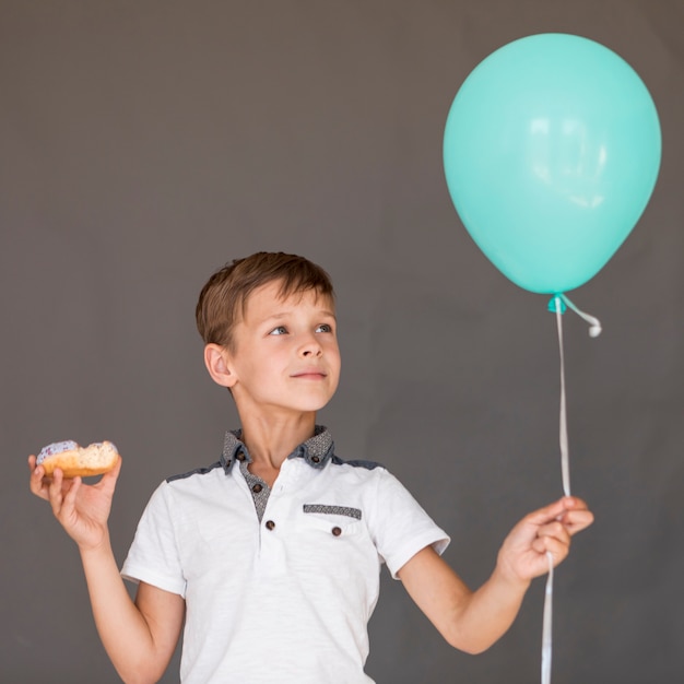 Vista frontal niño sosteniendo un globo y una rosquilla