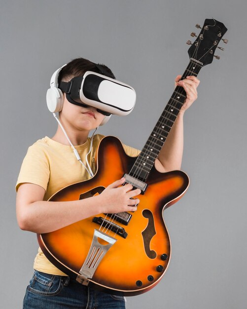 Vista frontal del niño tocando la guitarra mientras usa auriculares de realidad virtual