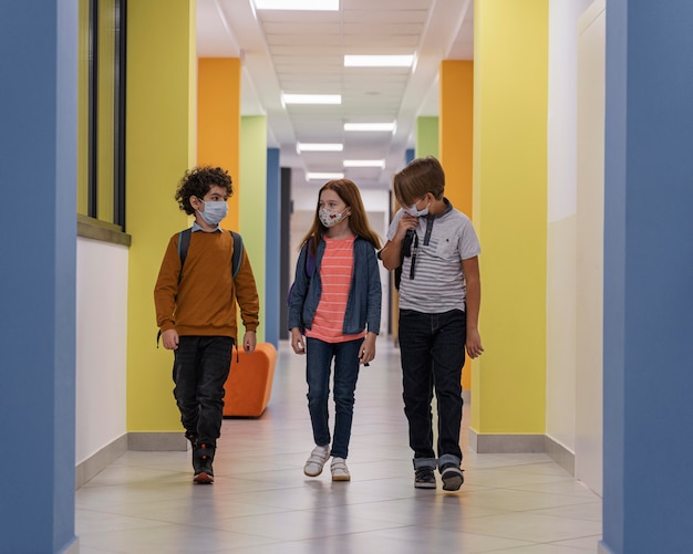 Vista frontal de los niños en el pasillo de la escuela con máscaras médicas