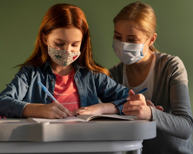 Vista frontal de niños que aprenden en la escuela con el maestro durante la pandemia de coronavirus