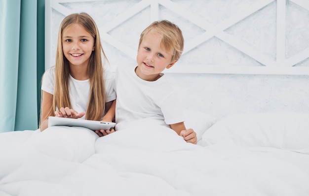 Vista frontal niños que se quedan en la cama mientras juegan en una tableta