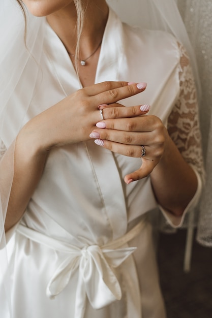 La vista frontal de una novia en la bata sedosa se pone el precioso anillo de compromiso