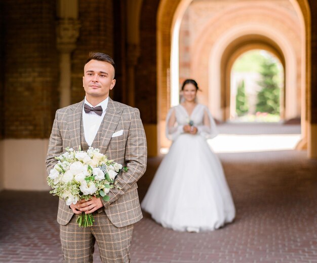 Vista frontal del novio pensativo y guapo en elegante traje a cuadros con ramo de flores mirando hacia otro lado mientras espera el primer encuentro con la novia